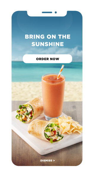 A mobile phone screen showcasing Tropical Smoothie Cafe Wrap, Chips & an Orange Smoothie arranged on a tray. A blurry beachy background with message “Bring on the Sunshine” and an Order Now button